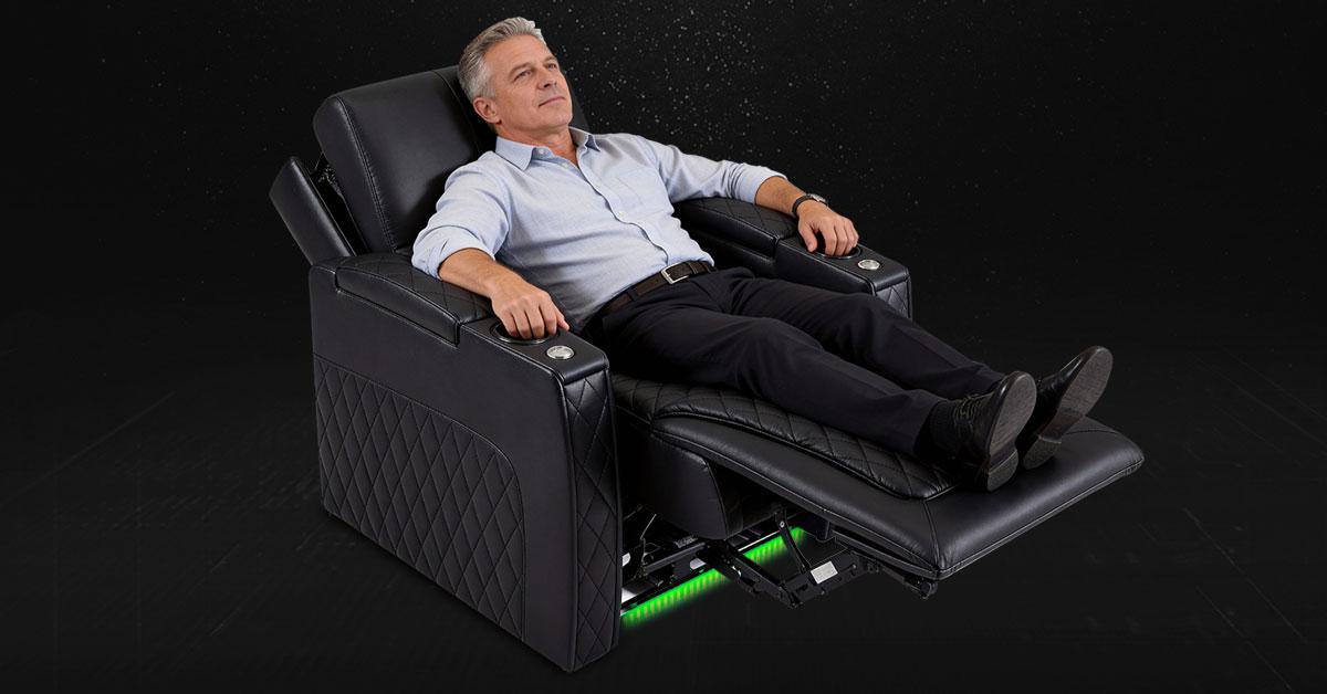 Man relaxing in a reclined black leather custom home theater chair with tray table and glowing LED base