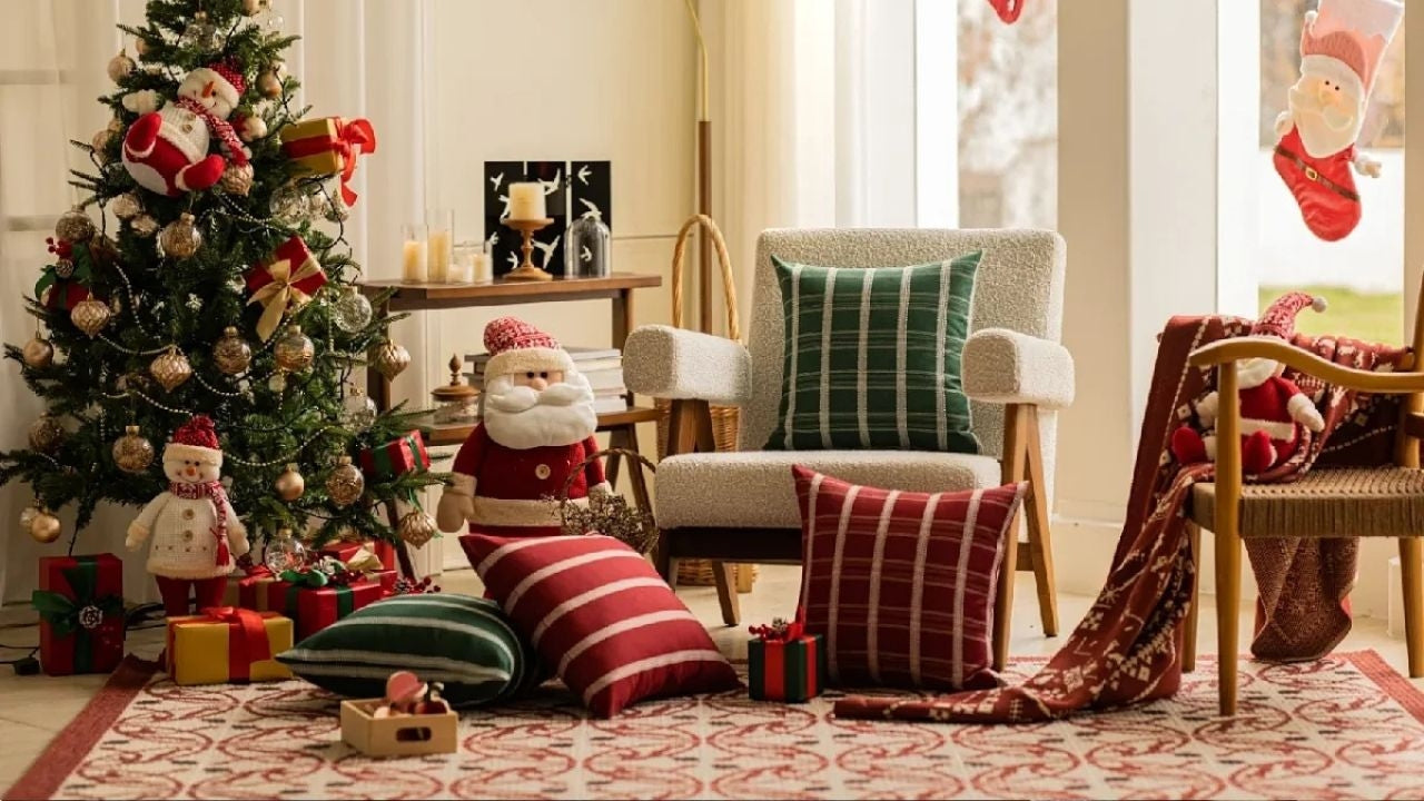 A festively decorated living room features a Christmas tree, Santa Claus dolls, wrapped presents, and pillows in holiday colors and patterns.