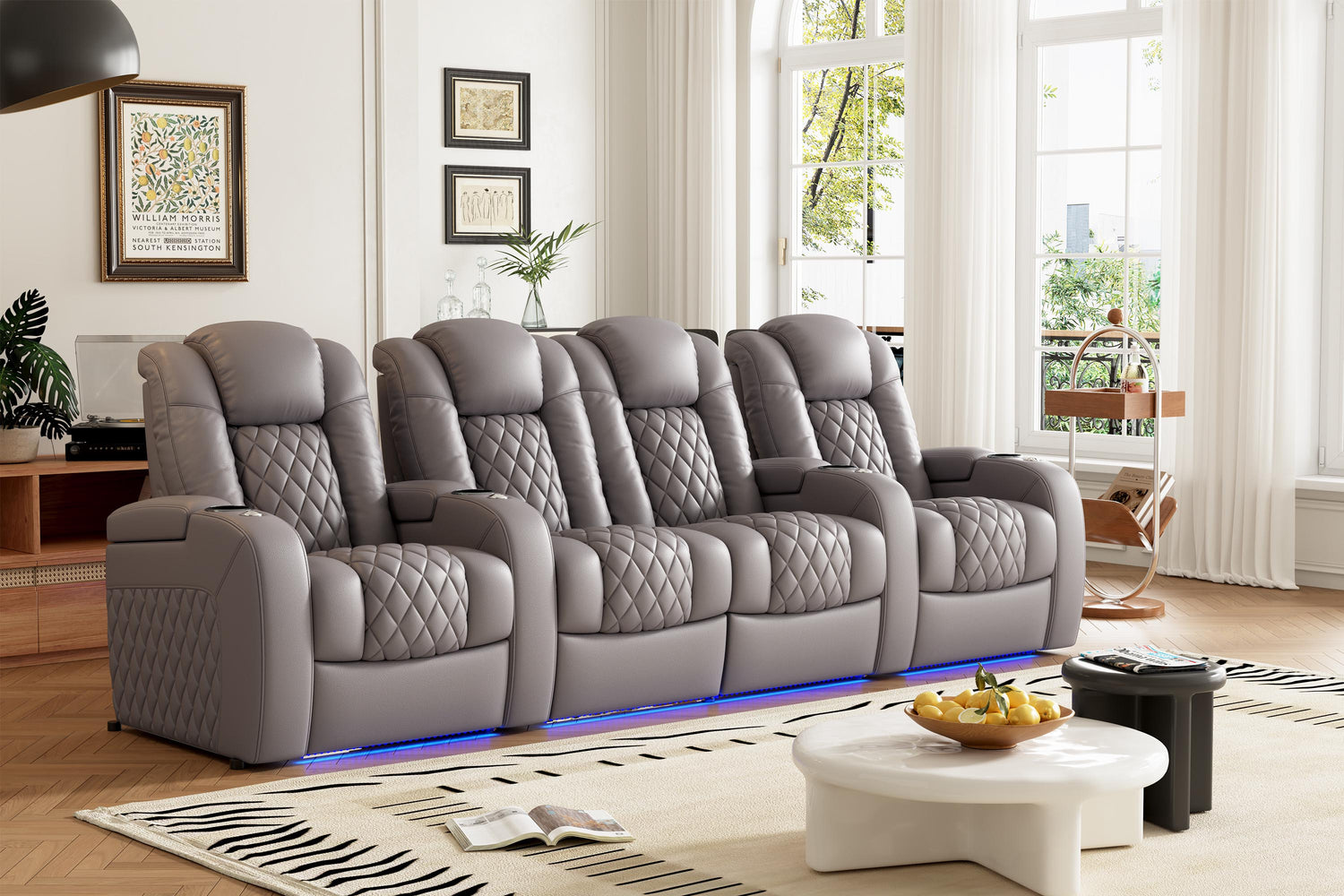 A four-seat home theater sofa in gray with diamond-quilted upholstery features LED base lighting, individual recliners, and cupholders, shown in a bright living room with hardwood floors and modern decor.