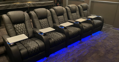 Row of luxury home theater seats with LED base lighting, swivel tables and premium leather upholstery design