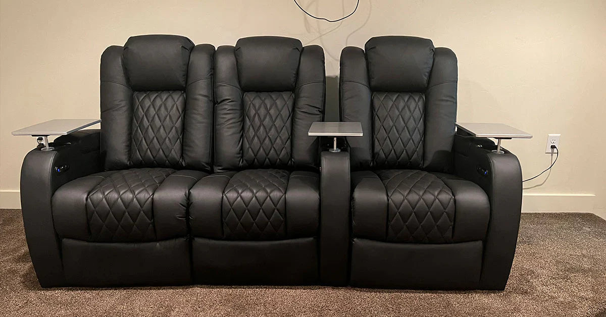 A row of black leather home theater recliners with diamond stitching and tray tables.