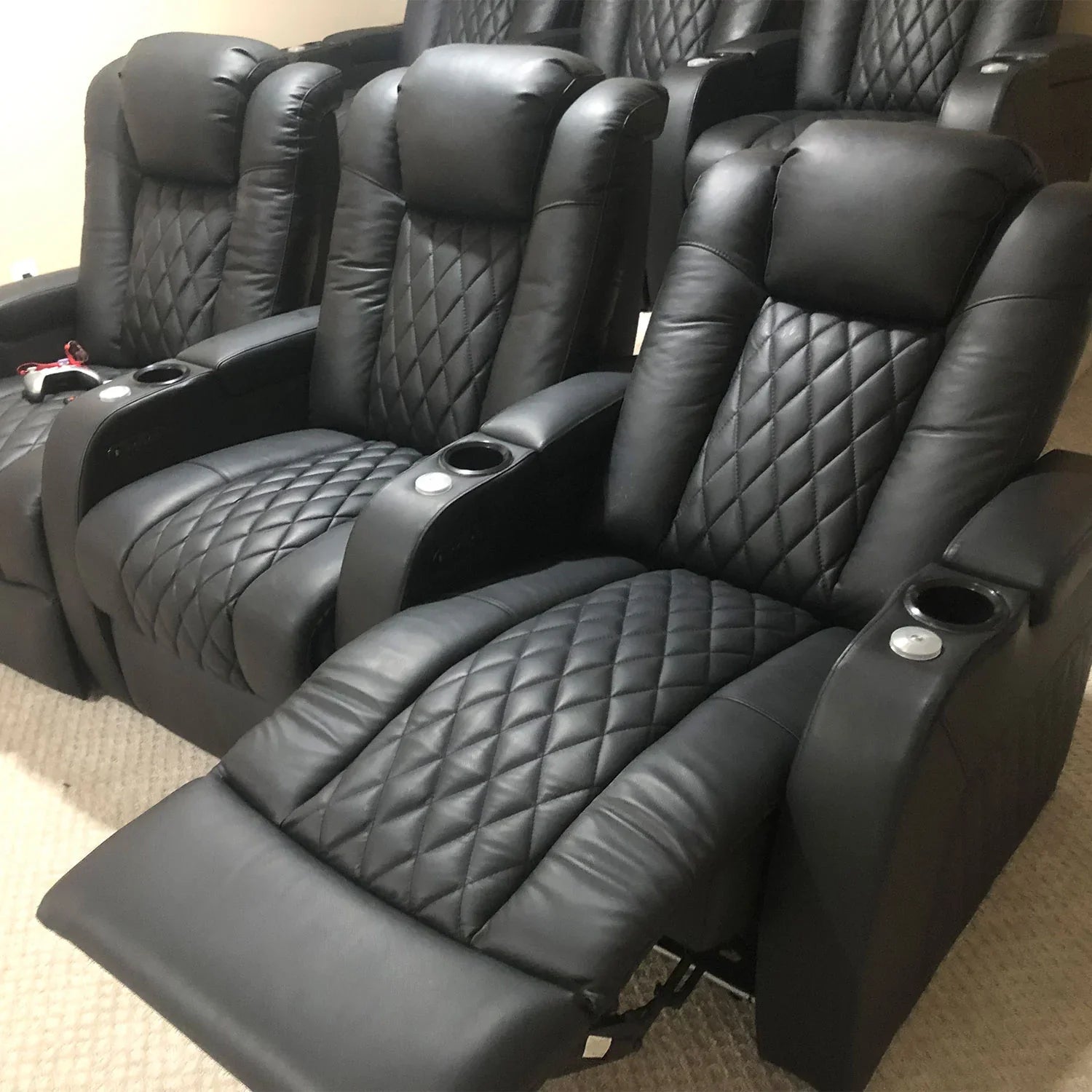 A row of three black, diamond-stitched leather power recliners in a reclined position.