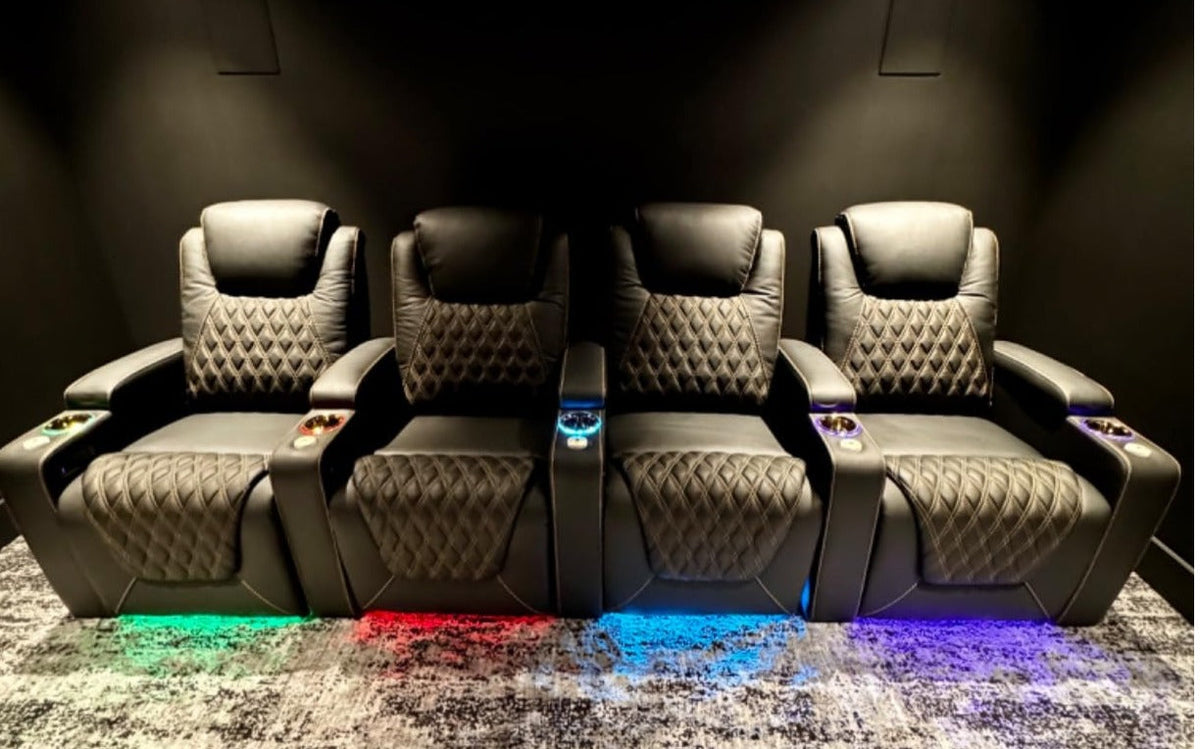 Row of four black leather home theater seats with diamond stitching and colorful LED underglow.