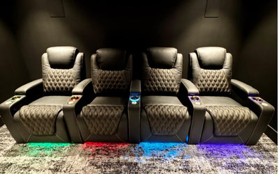 Row of four black leather home theater seats with diamond stitching and colorful LED underglow.