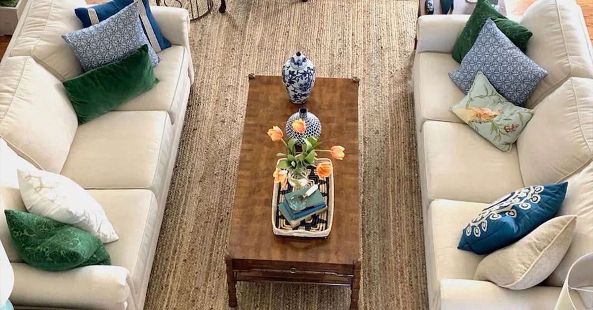 U-shaped sectional layout with botanical pillows on woven rug, tray with orange tulips centerpiece.