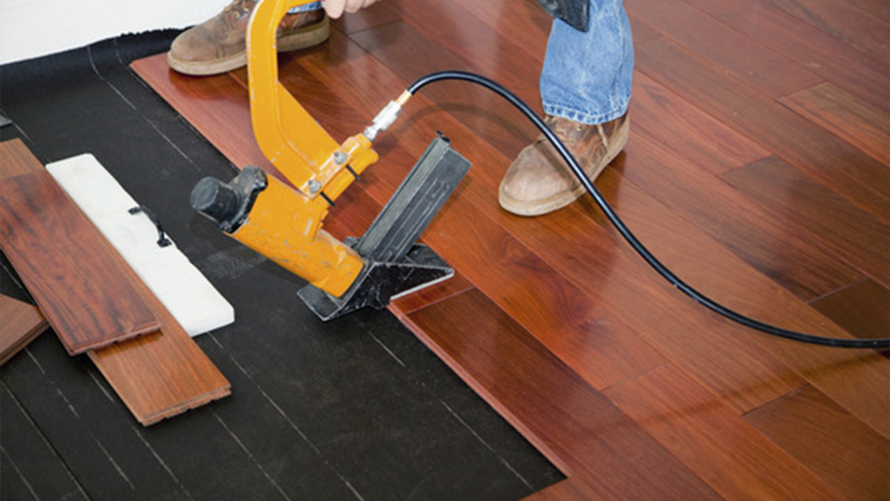 Installing hardwood flooring with a nail gun.